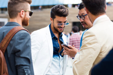 Stylish men outside discussing phone.