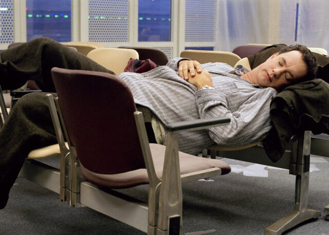 Person sleeps on airport seats; serene terminal.