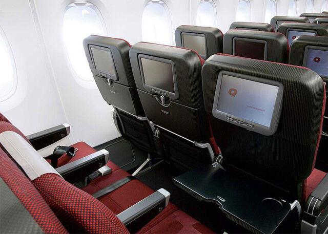Airplane cabin with red seats and screens.