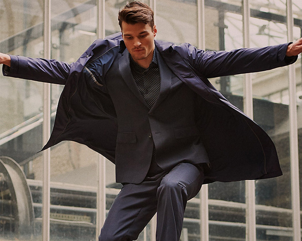 Man in dark suit jumps before glass structure.