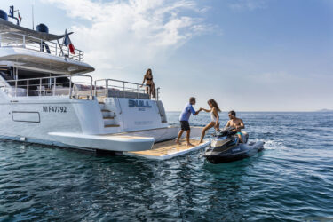 Man helps woman onto yacht "Bull," idyllic Mediterranean scene.