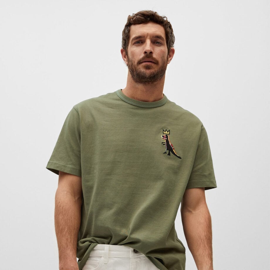 Man with curly hair wears dinosaur crown T-shirt.