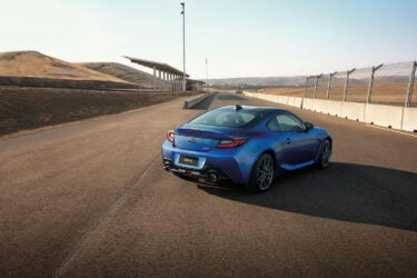 Blue Subaru BRZ on empty track, hills visible.
