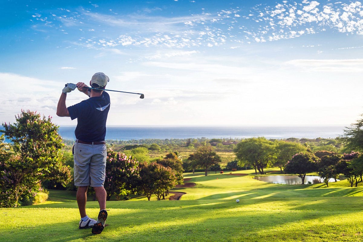 Golfer mid-swing on scenic course.