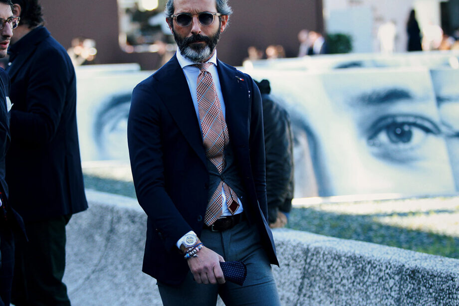 Grey-haired man ties checkered tie.