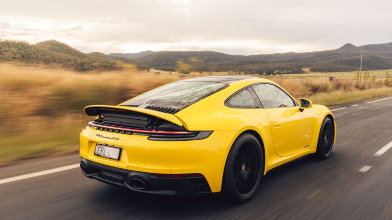 Yellow Porsche 911 GTS speeds through scenic landscape.