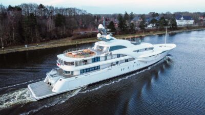A superyacht sails calmly amidst forest and buildings.