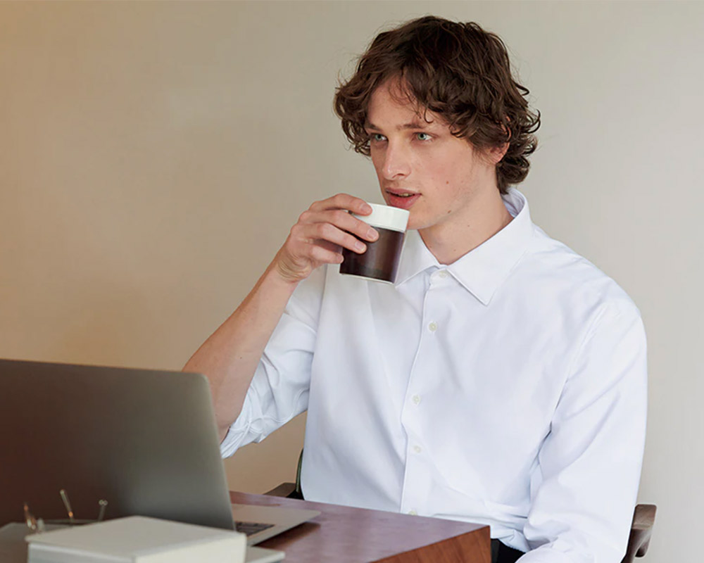 Curly-haired professional works at desk, sipping coffee.