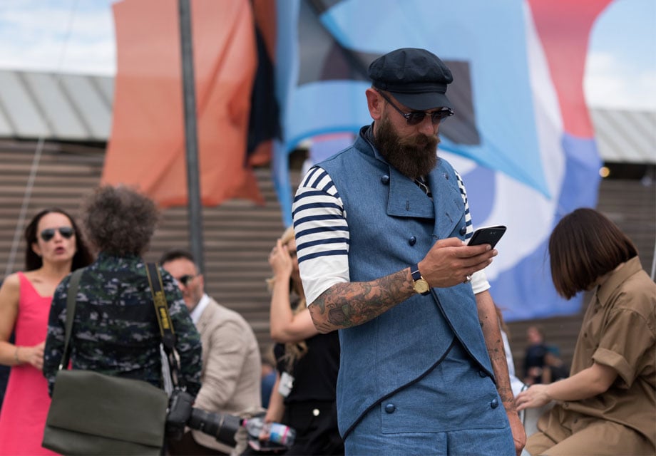 Bearded man checks phone, crowd.