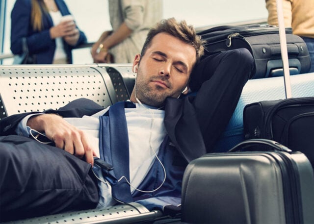 Tired businessman naps on airport bench.