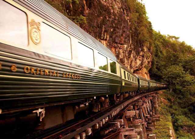 A luxury train glides beside a cliff.